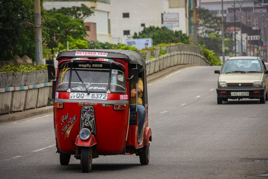 Red tuk-tuk taxi driving on an urban road, showcasing public transport in action.