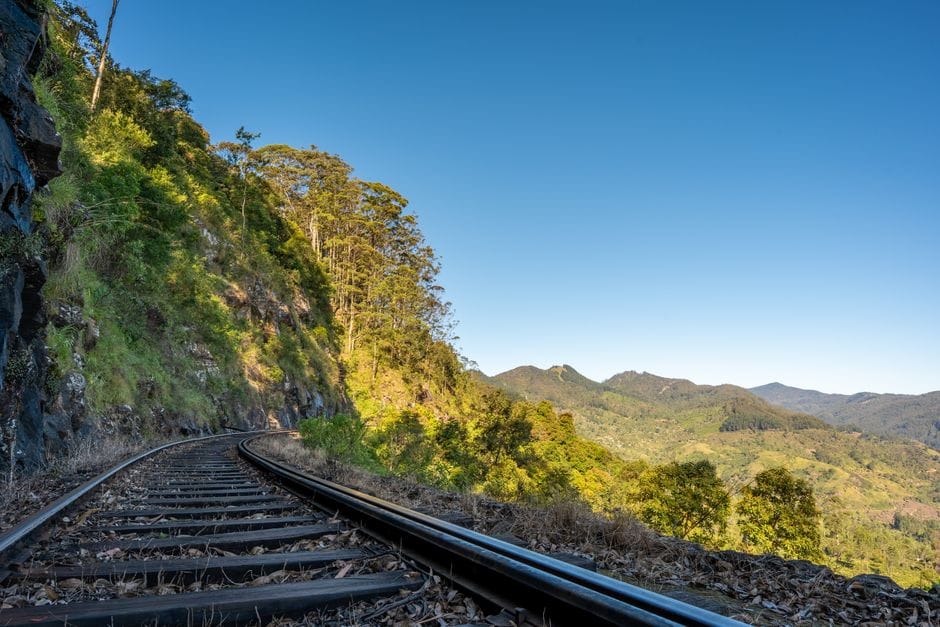 Curved railway tracks through lush hills in Sri Lanka on a clear day.